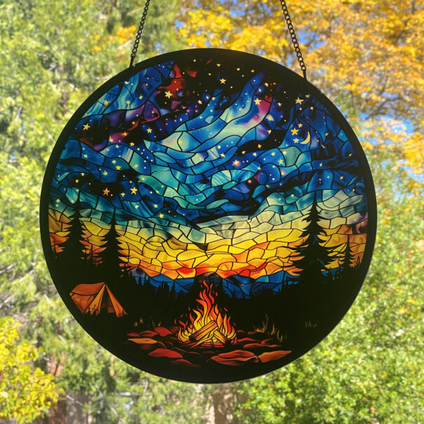 Round stained glass image of a campfire under a starry sky.