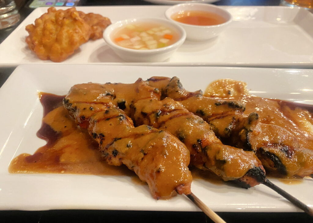 Plate of chicken satay, covered with peanut sauce.